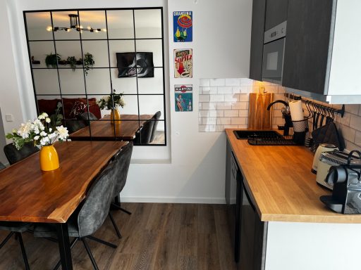 Moderne Küche mit Holzarbeitsfläche, Esstisch und Pflanzen im Hintergrund.